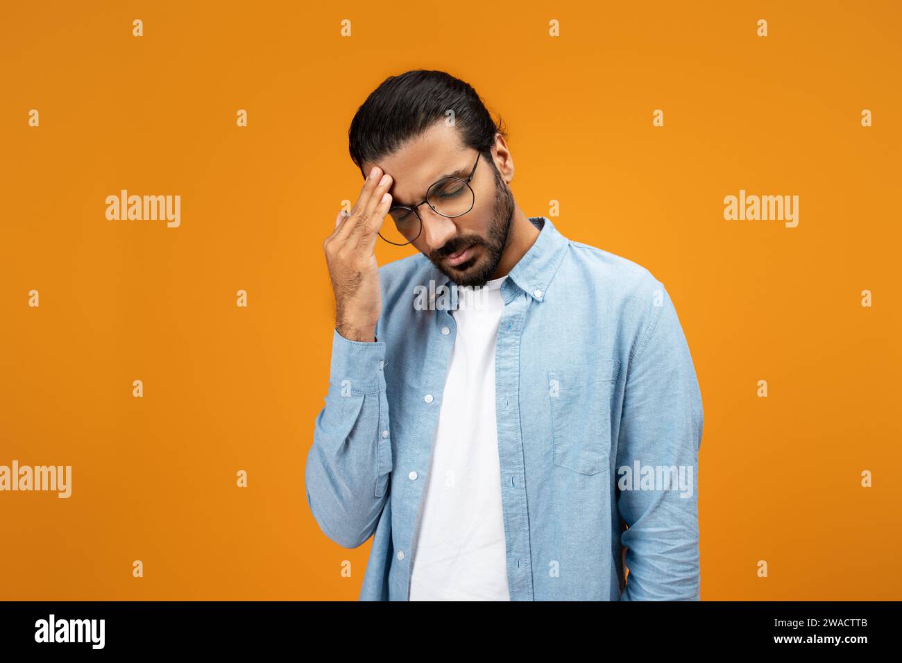 Un uomo pensivo con una camicia in denim azzurro tocca la fronte, mostrando un gesto di preoccupazione Foto Stock