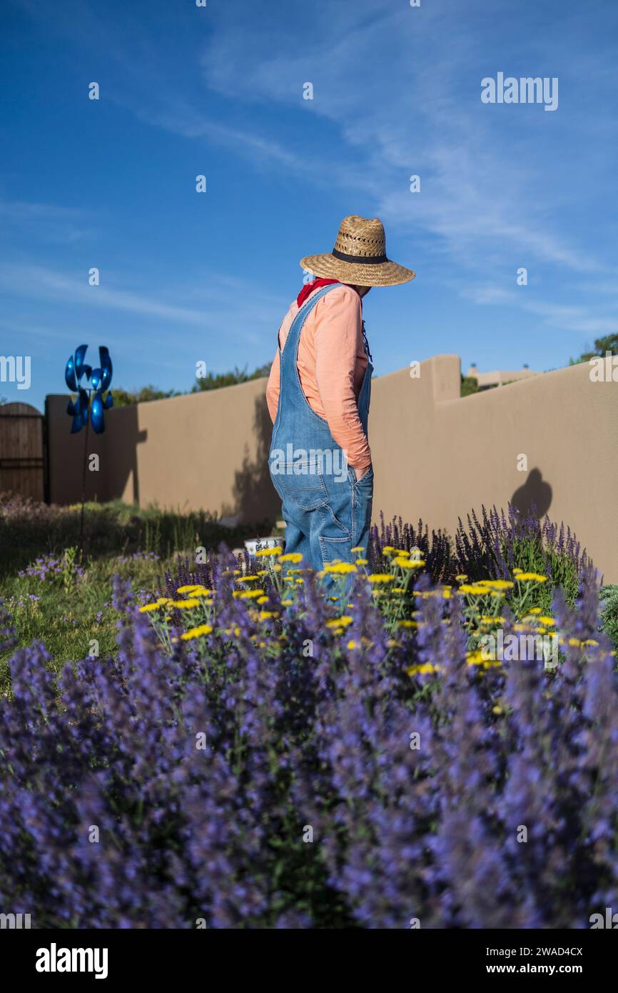 USA, New Mexico, Santa Fe, donna con cappello di paglia e tute in denim in giardino Foto Stock