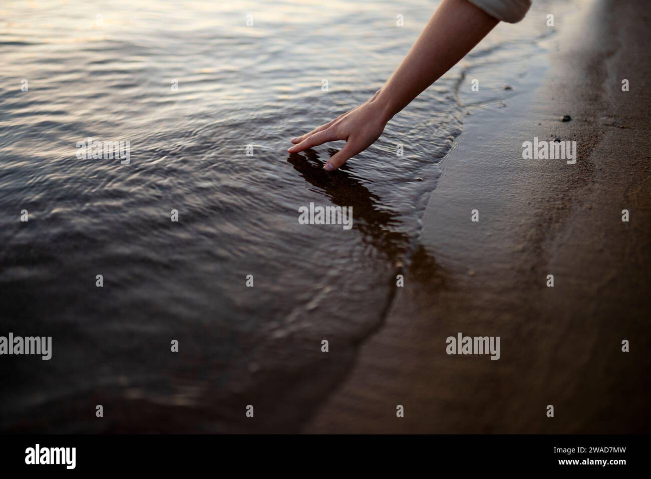 Primo piano di una donna che tocca l'acqua nel fiume al tramonto Foto Stock
