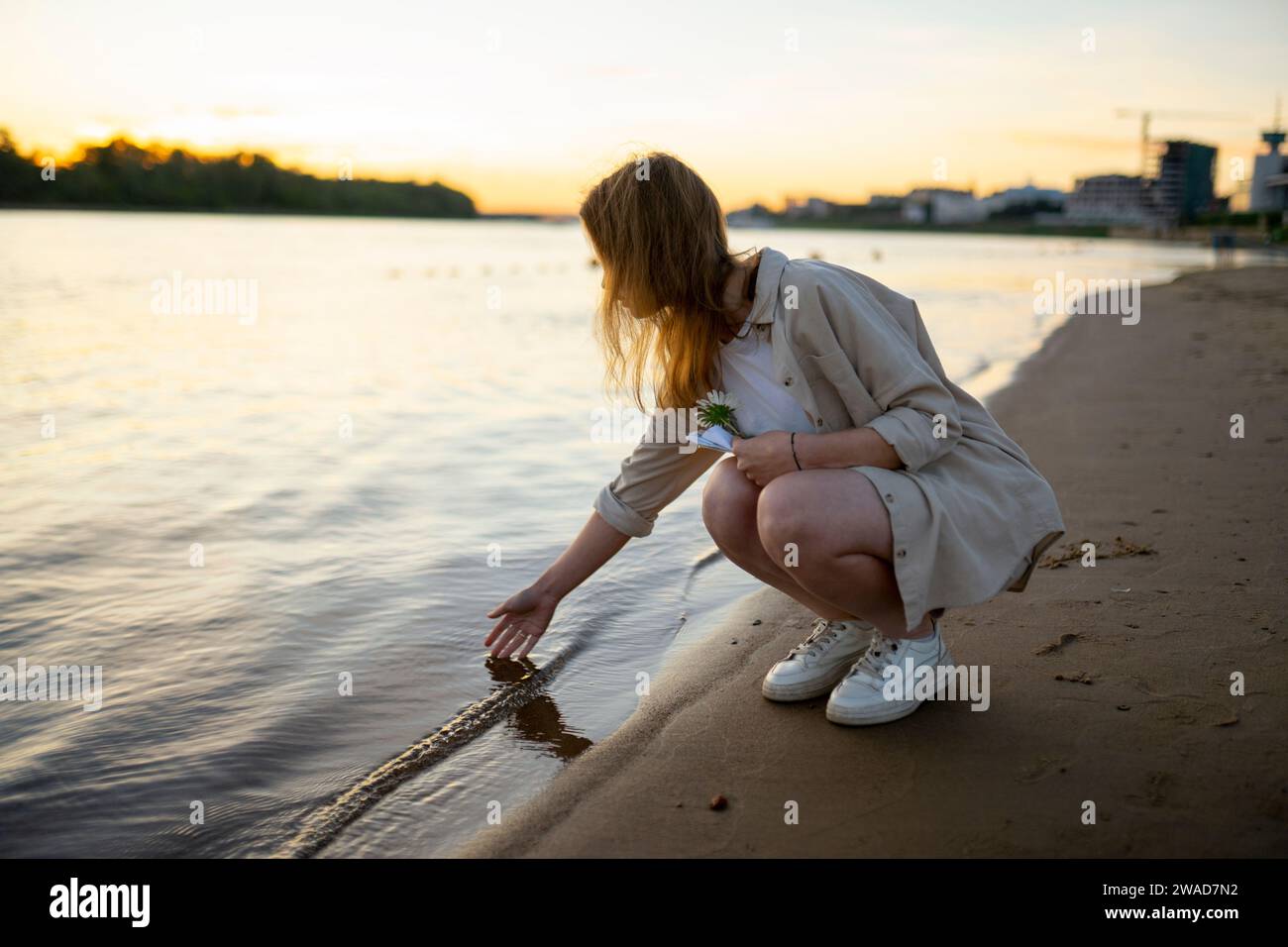 Donna che tocca l'acqua nel fiume al tramonto Foto Stock