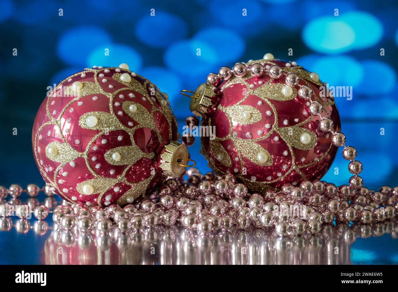 Un paio di bauble dell'albero di Natale rosso e oro, fotografati con una collana con perline bianche, su sfondo blu Foto Stock