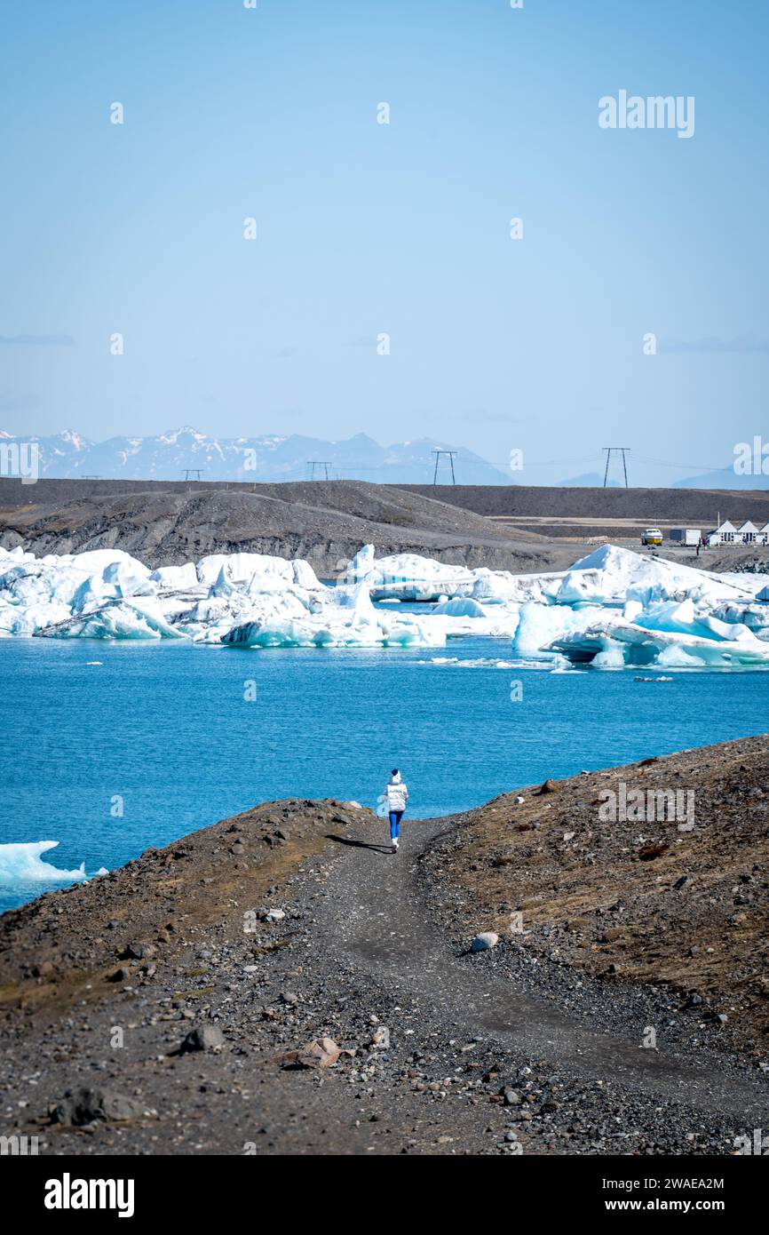 Una persona sta passeggiando in un ambiente pittoresco, con iceberg che brillano alla luce del sole vicino a un corpo d'acqua Foto Stock