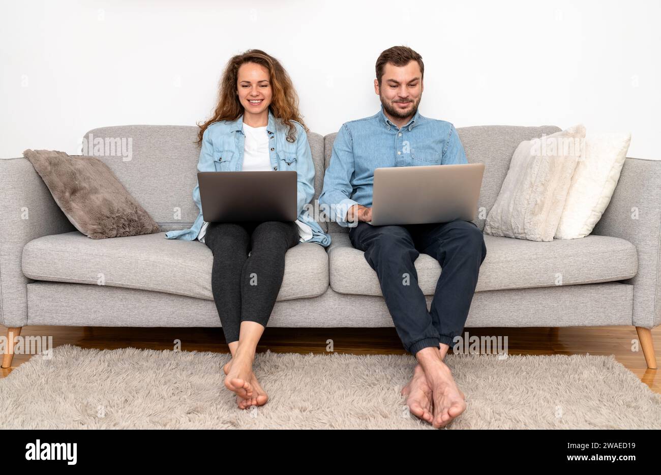 Due persone, un uomo e una donna, sedute insieme su un divano, sorridendo e lavorando su un notebook. Formazione e apprendimento online. Foto Stock