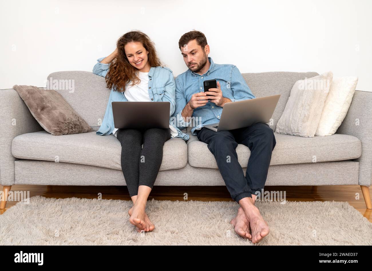 Due persone, donna e uomo seduti sul divano a casa, usano i loro dispositivi digitali. Foto Stock
