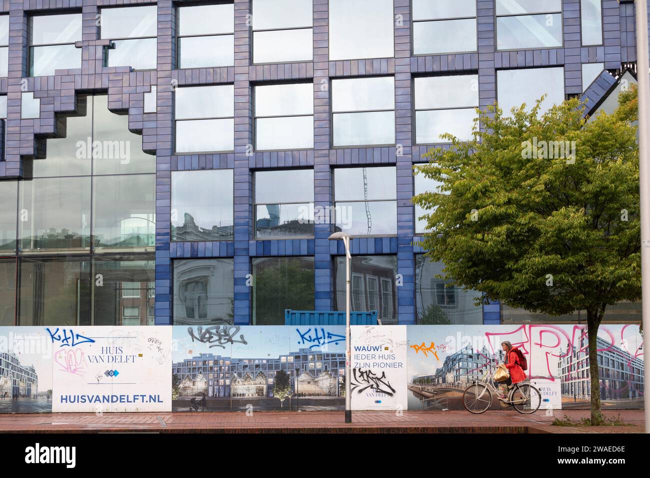 Ciclista che passa la nuova costruzione di un edificio multifunzionale chiamato 'huis van Delft' nei colori delftware nel centro della città di Delft Foto Stock
