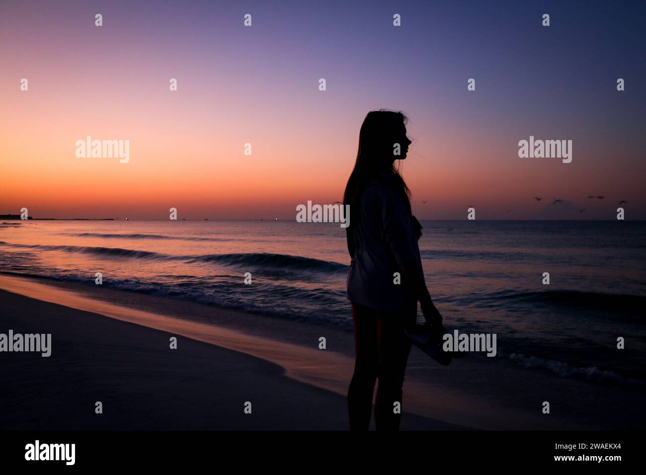 Una silhouette di una giovane donna in piedi sulla riva di una spiaggia al tramonto a Destin, Florida Foto Stock