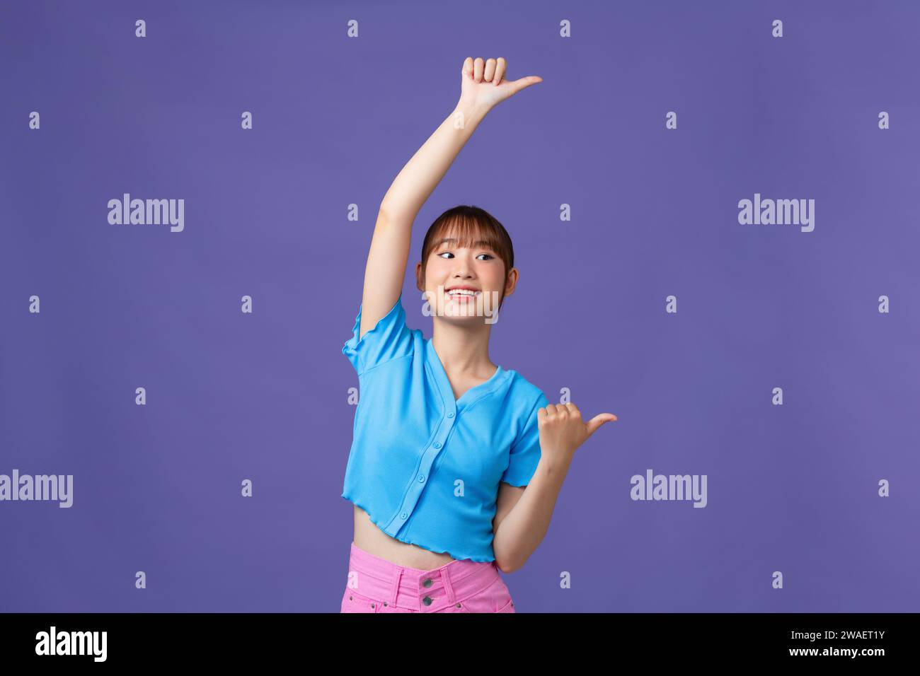 Giovane donna asiatica sorridente con faccia felice che guarda e punta da parte con il dito in alto. Foto Stock