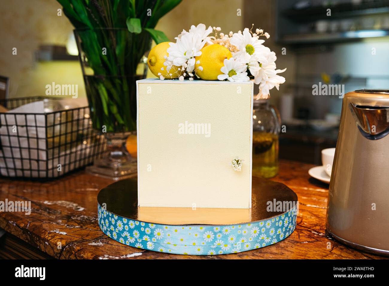 Un primo piano del banco in marmo di un caffè che presenta una torta contemporanea con limoni e fiori bianchi, accentuando un'atmosfera accogliente ed elegante. Foto Stock