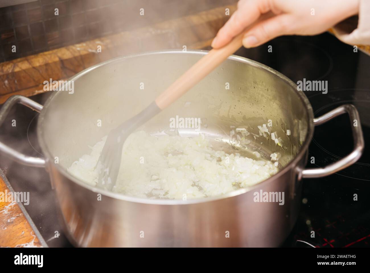 Uno chef salta le cipolle tagliate a dadini in una pentola in acciaio inox sopra un fornello, i primi passi di una preparazione gustosa del pasto. Foto Stock
