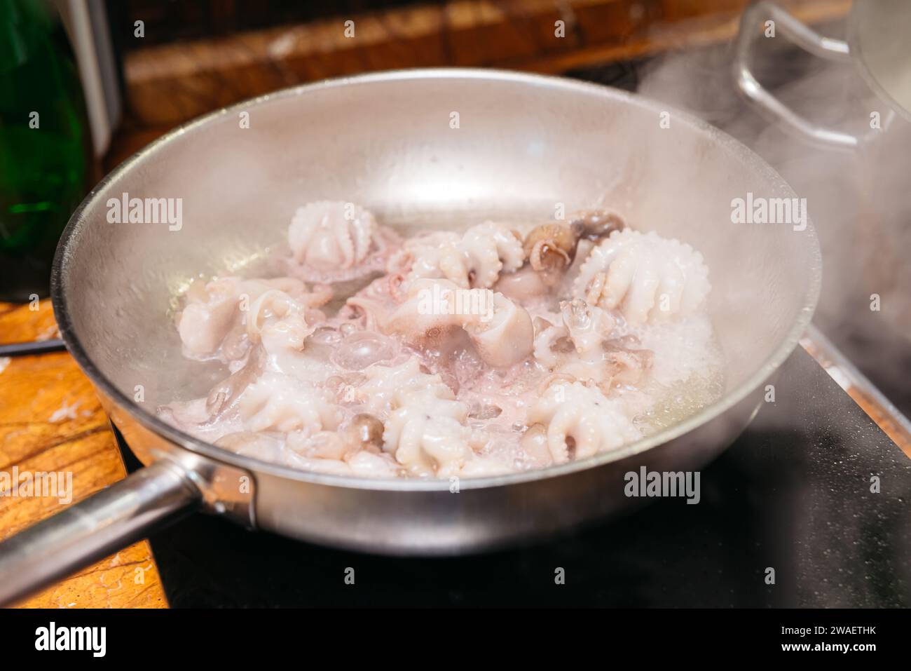 Una padella in acciaio inox sulla stufa con acqua bollente e polpo piccolo, un passo nella preparazione di un piatto a base di pesce. Foto Stock