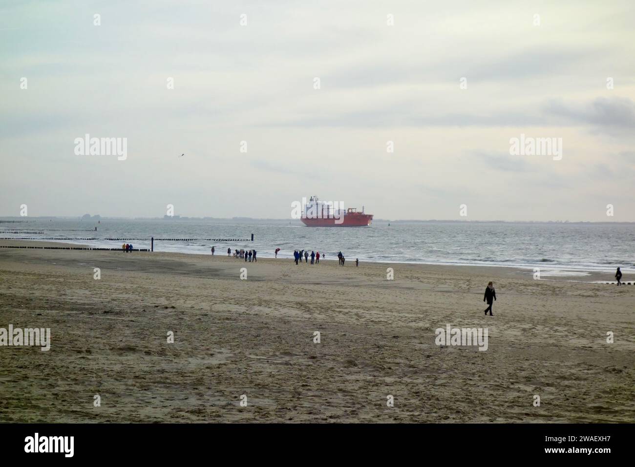 Una grande barca a vela che passa accanto a un gruppo di persone che si stendono tranquillamente su una spiaggia sabbiosa Foto Stock