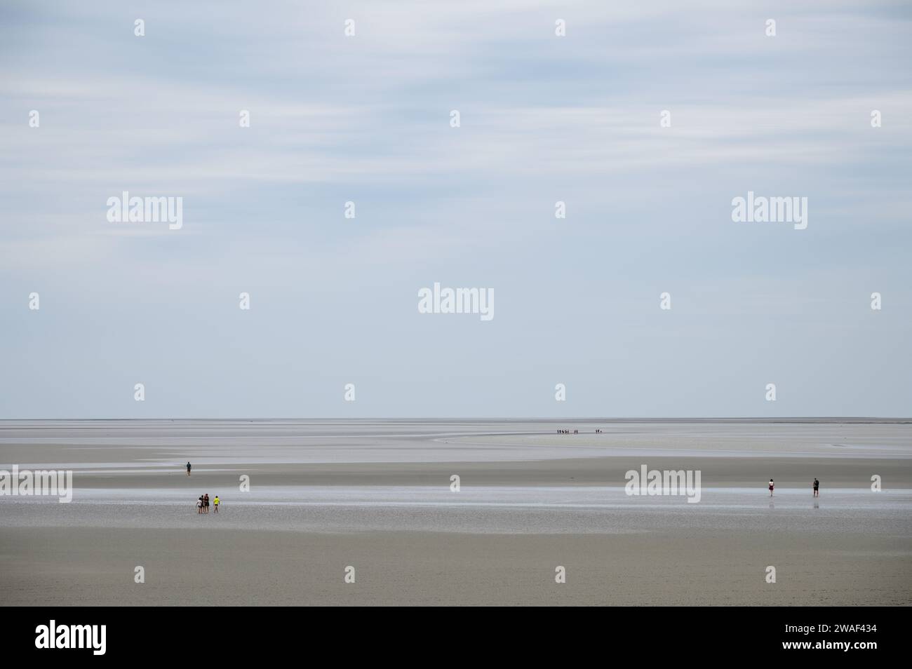 Paesaggio di bassa marea con la sabbia vicino a Mont Saint-Michel con alcune sagome di turisti sullo sfondo che visitano il luogo Foto Stock