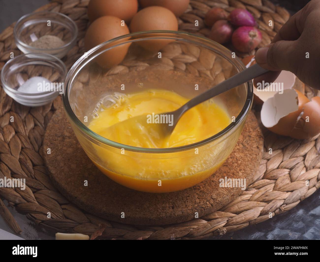mescolare a mano le uova in un recipiente di vetro con una forchetta, ingredienti come uova di fondo, cipolla rossa, sale e papper Foto Stock