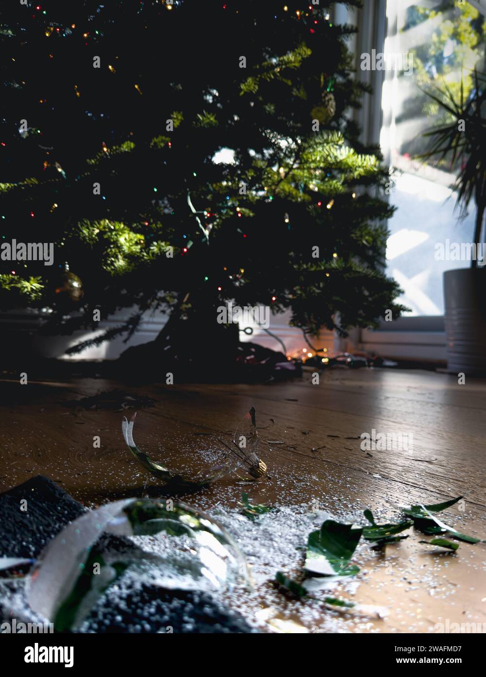 Bauble natalizio in vetro frantumato sul pavimento del soggiorno con l'albero di Natale sullo sfondo Foto Stock