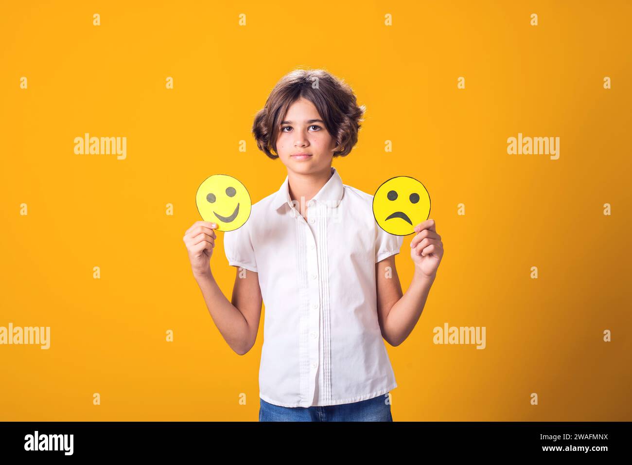 La ragazza tiene in mano emoticon tristi e felici. Concetto di salute mentale, psicologia ed emozioni dei bambini Foto Stock