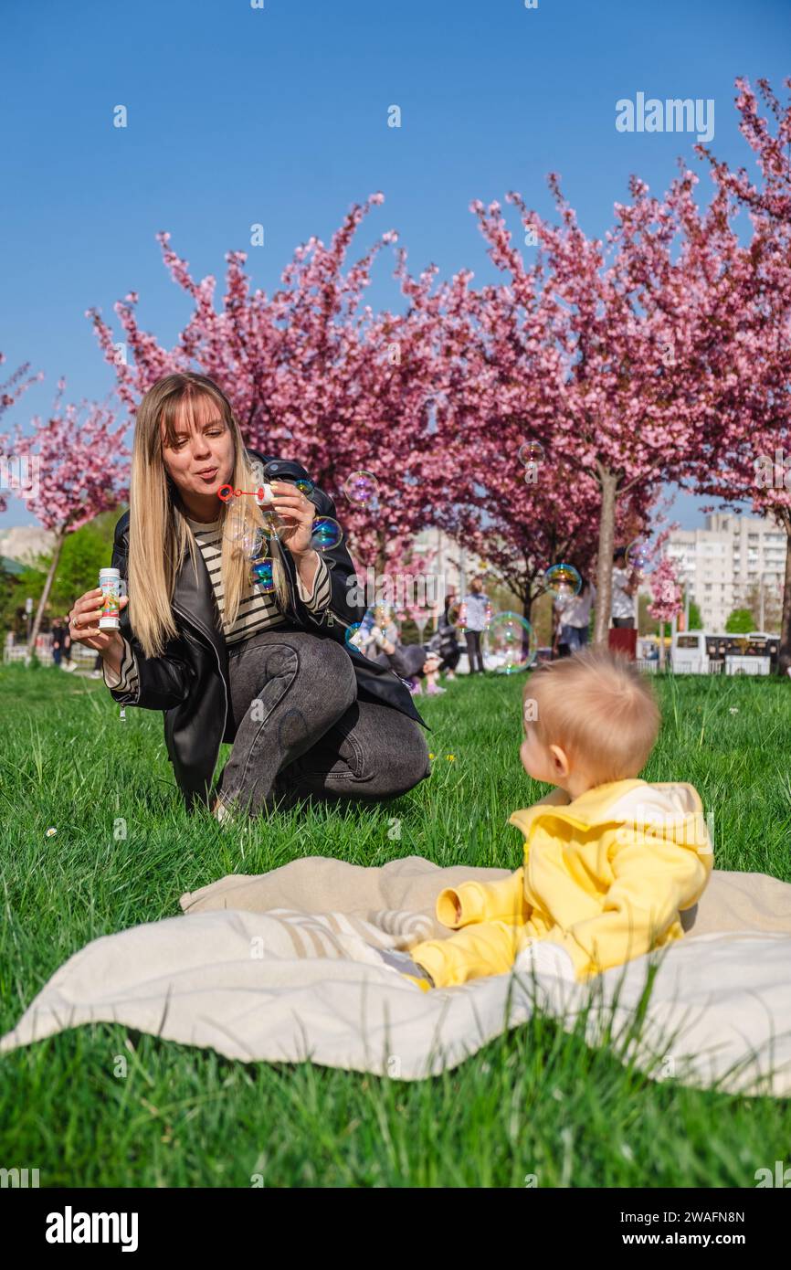 Mamma e figlio gioiosi stanno giocando con le bolle vicino ai ciliegi in fiore Foto Stock