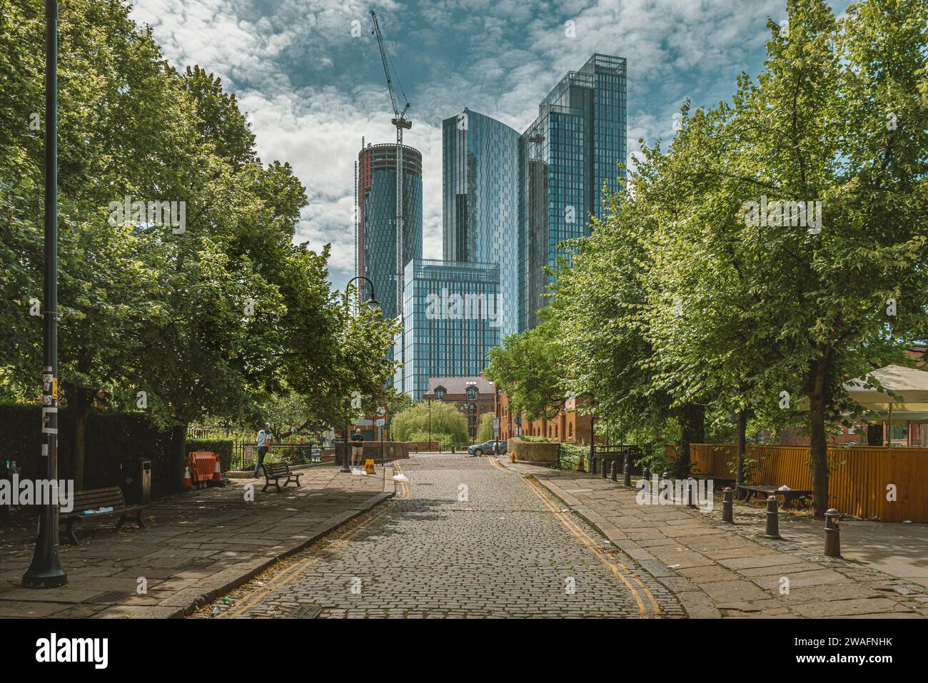Una strada acciottolata alberata conduce l'occhio dall'architettura tradizionale all'architettura contemporanea dei grattacieli di Manchester. Foto Stock