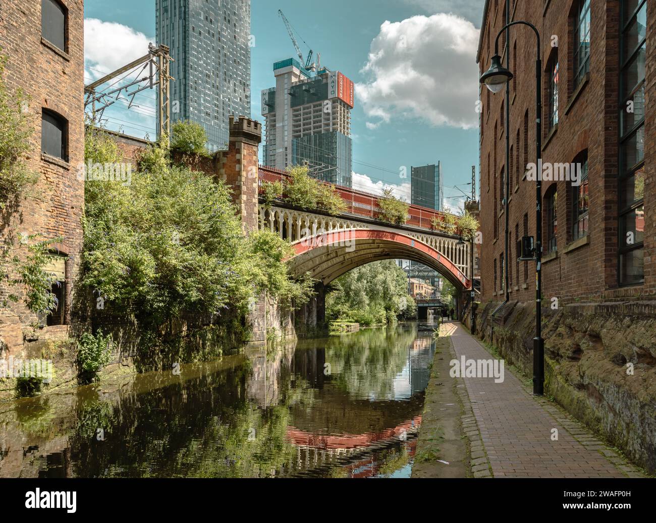 Un ponte vittoriano riflesso nel canale di Rochdale. Dietro di esso, si innalzano i grattacieli contemporanei che mostrano l'evoluzione della città di Manchester. Foto Stock