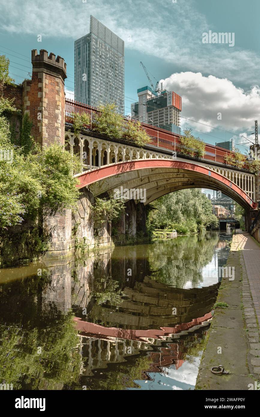 Un ponte vittoriano riflesso nel canale di Rochdale. Dietro di esso, si innalzano i grattacieli contemporanei che mostrano l'evoluzione della città di Manchester. Foto Stock