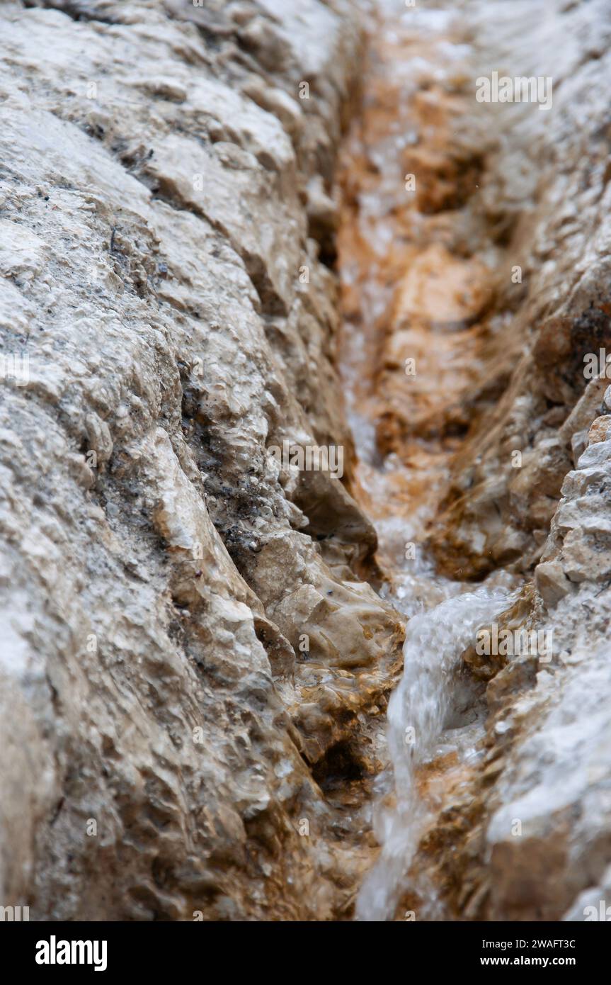 Un piccolo torrente scorre tra rocce calcaree brune ferruginose. Sfocatura movimento. Profondità di campo ridotta. Immagine di sfondo Foto Stock