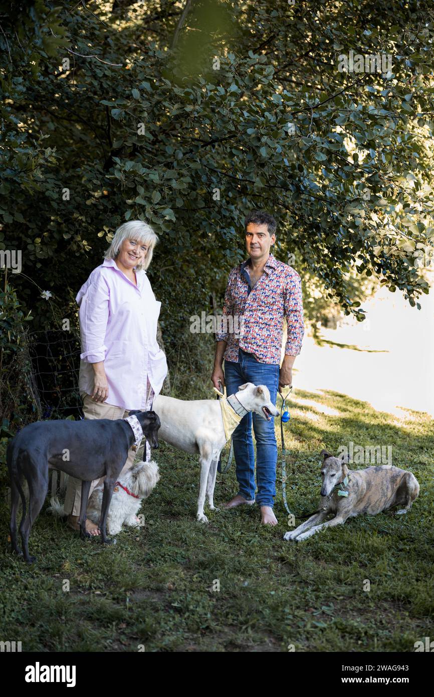 Un paio di uomini e donne in posa nel campo che si godono i levrieri nel campo, foto verticale Foto Stock