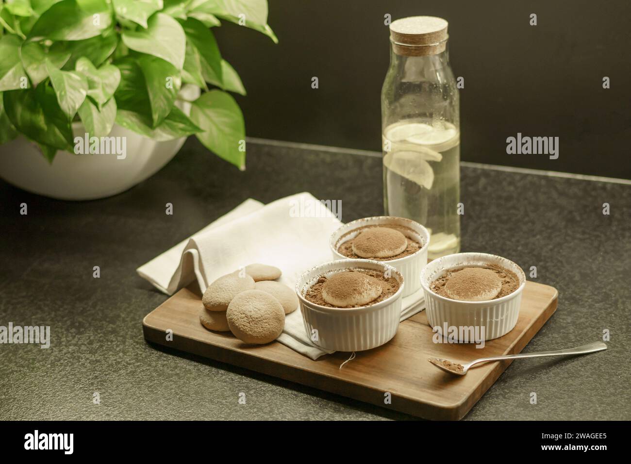 ciotole con tiramisù fatto in casa su una tavola di legno, cucchiaio con cacao in polvere, torte di spugna e un panno Foto Stock
