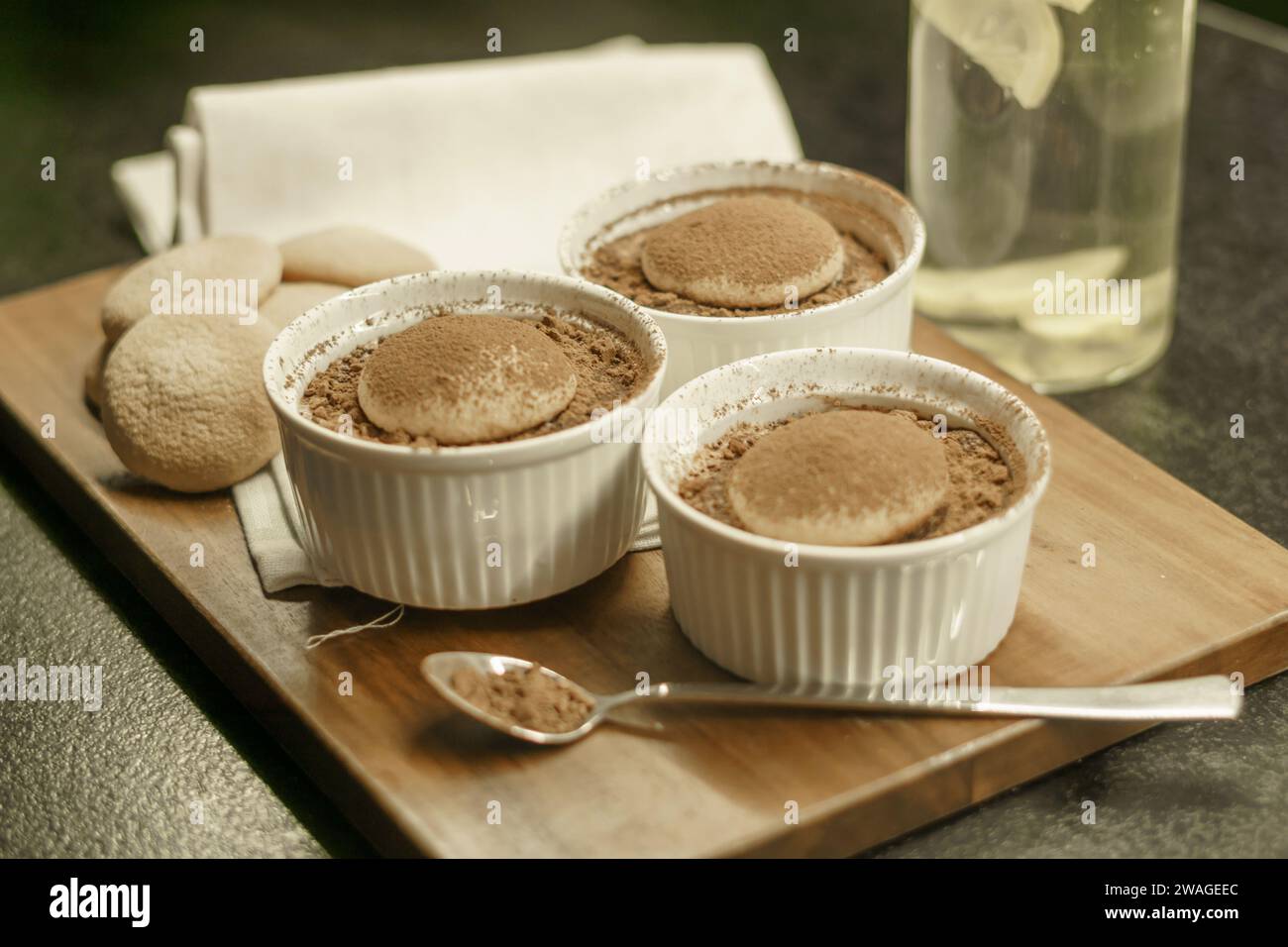 ciotole con tiramisù fatto in casa su una tavola di legno, cucchiaio con cacao in polvere, torte di spugna e un panno Foto Stock