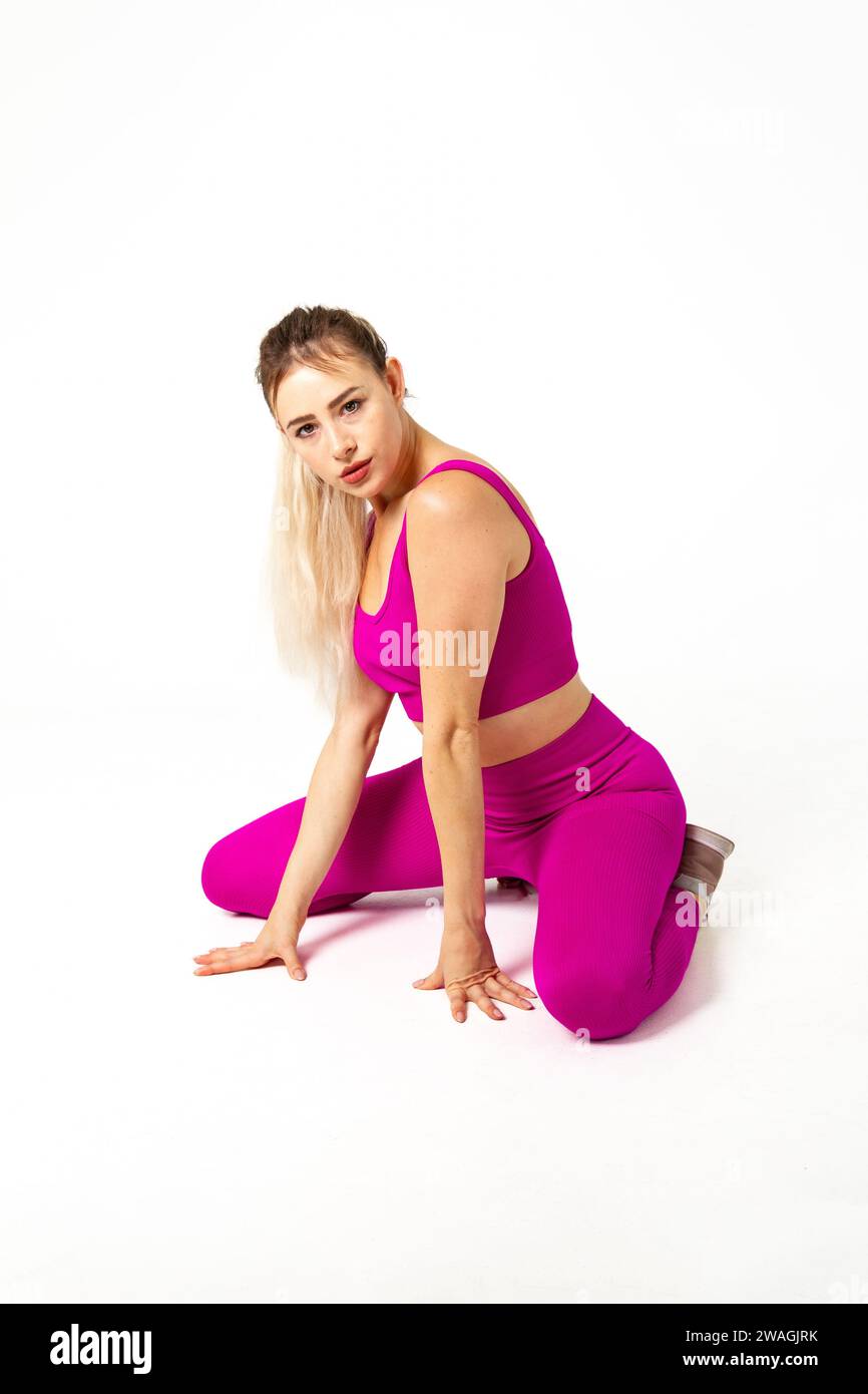 Donna con un vivace outfit sportivo rosa, ginocchia e mani sul pavimento Foto Stock