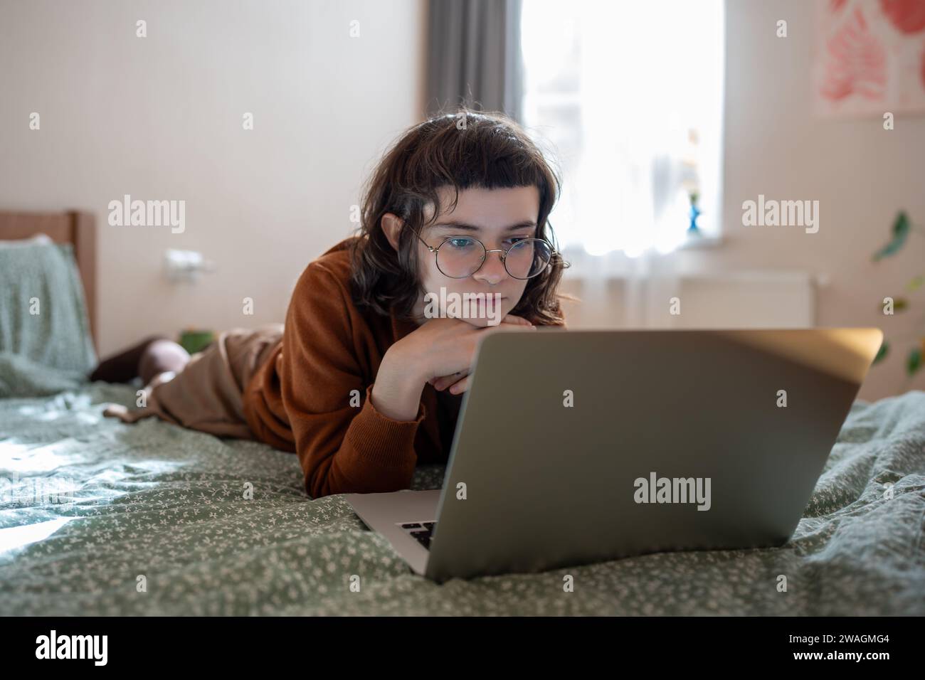 Ragazza adolescente interessata che passa il fine settimana, passeggia a casa, guarda video, filma su un computer portatile Foto Stock