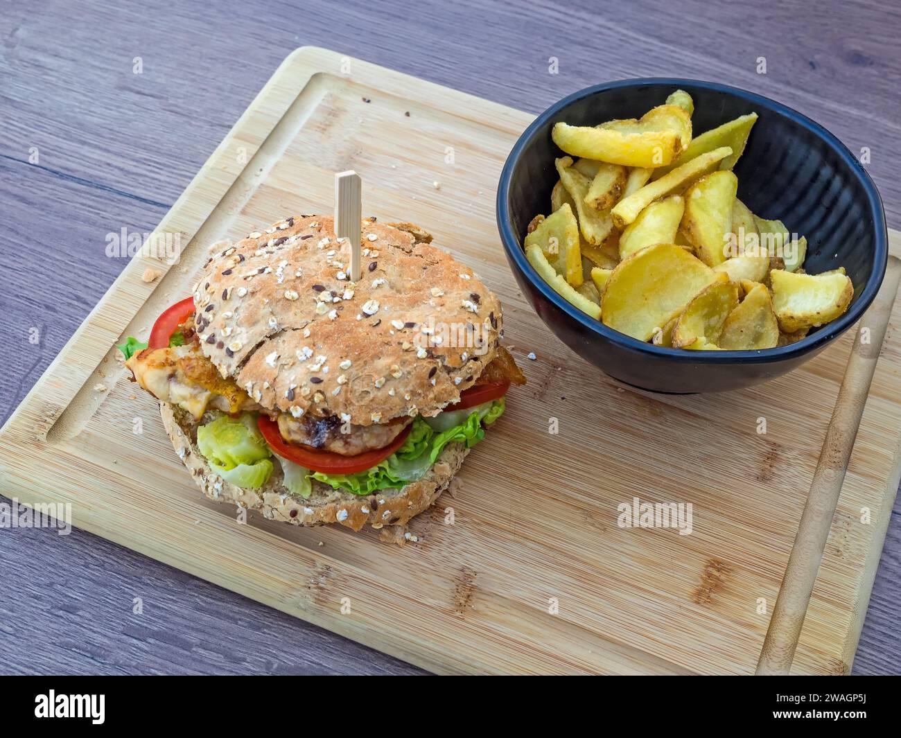 Succulento hamburger di pesce con patatine fritte servito su un asse di legno Foto Stock