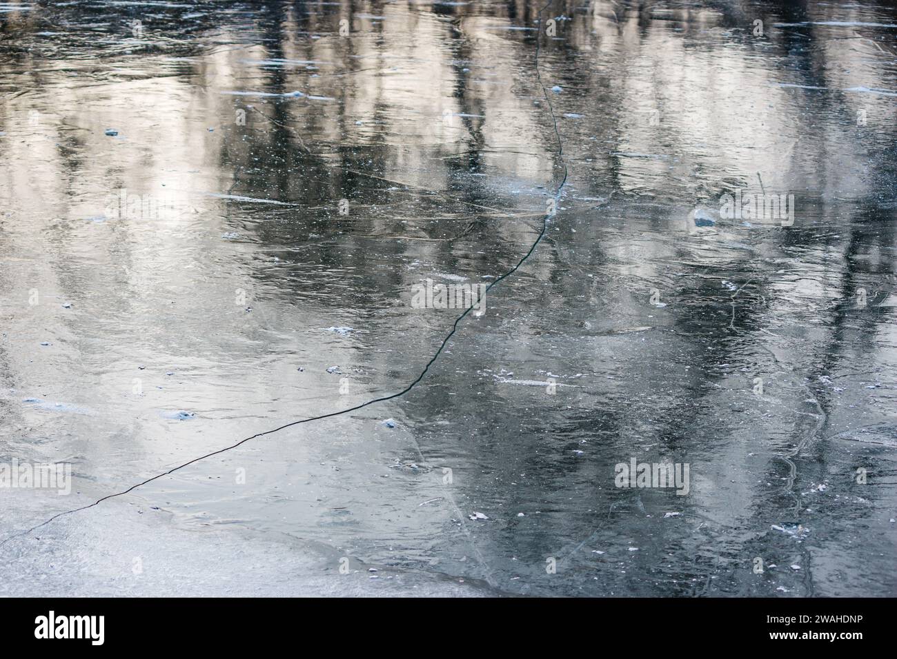 Grosse crepe su ghiaccio grigio al centro di uno stagno Foto Stock