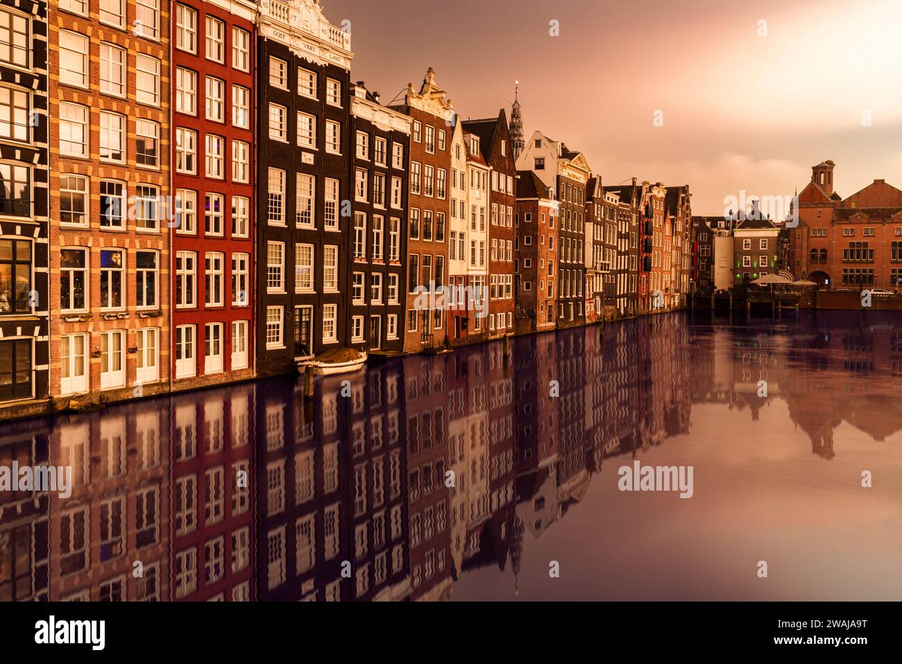Riflessi dell'ora d'oro sull'acqua con una fila di case tradizionali olandesi colorate lungo il canale di Amsterdam Foto Stock