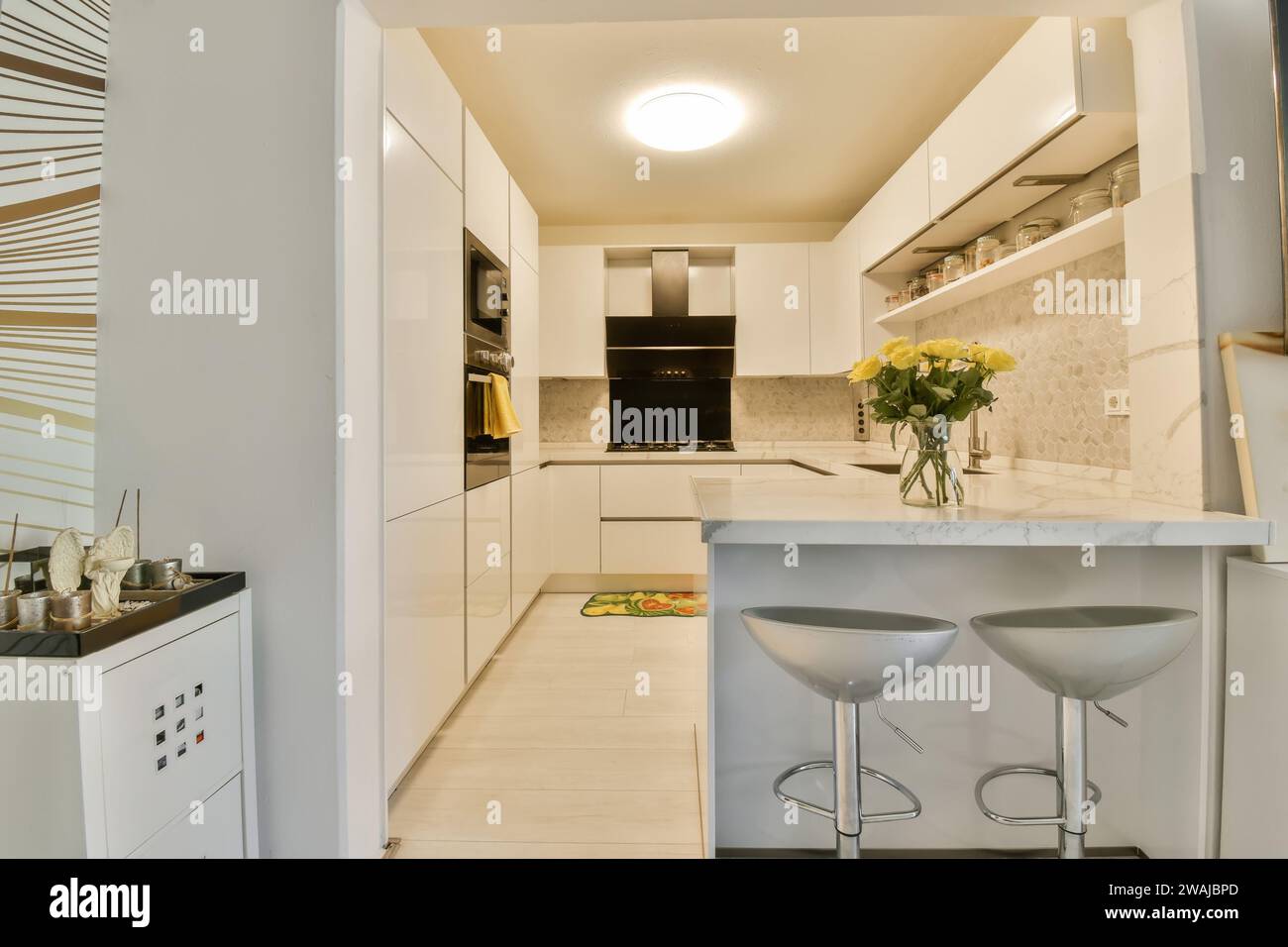 Elettrodomestici moderni con armadi bianchi e sgabello collocati da un bancone in marmo in una moderna cucina illuminata a casa Foto Stock