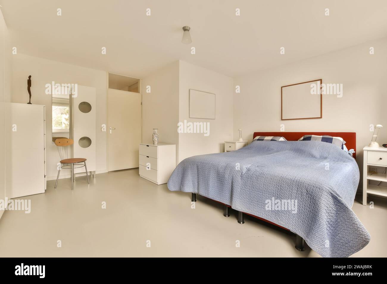 Interno di una spaziosa camera da letto con grande e comodo letto blu e comò in un appartamento moderno e luminoso Foto Stock
