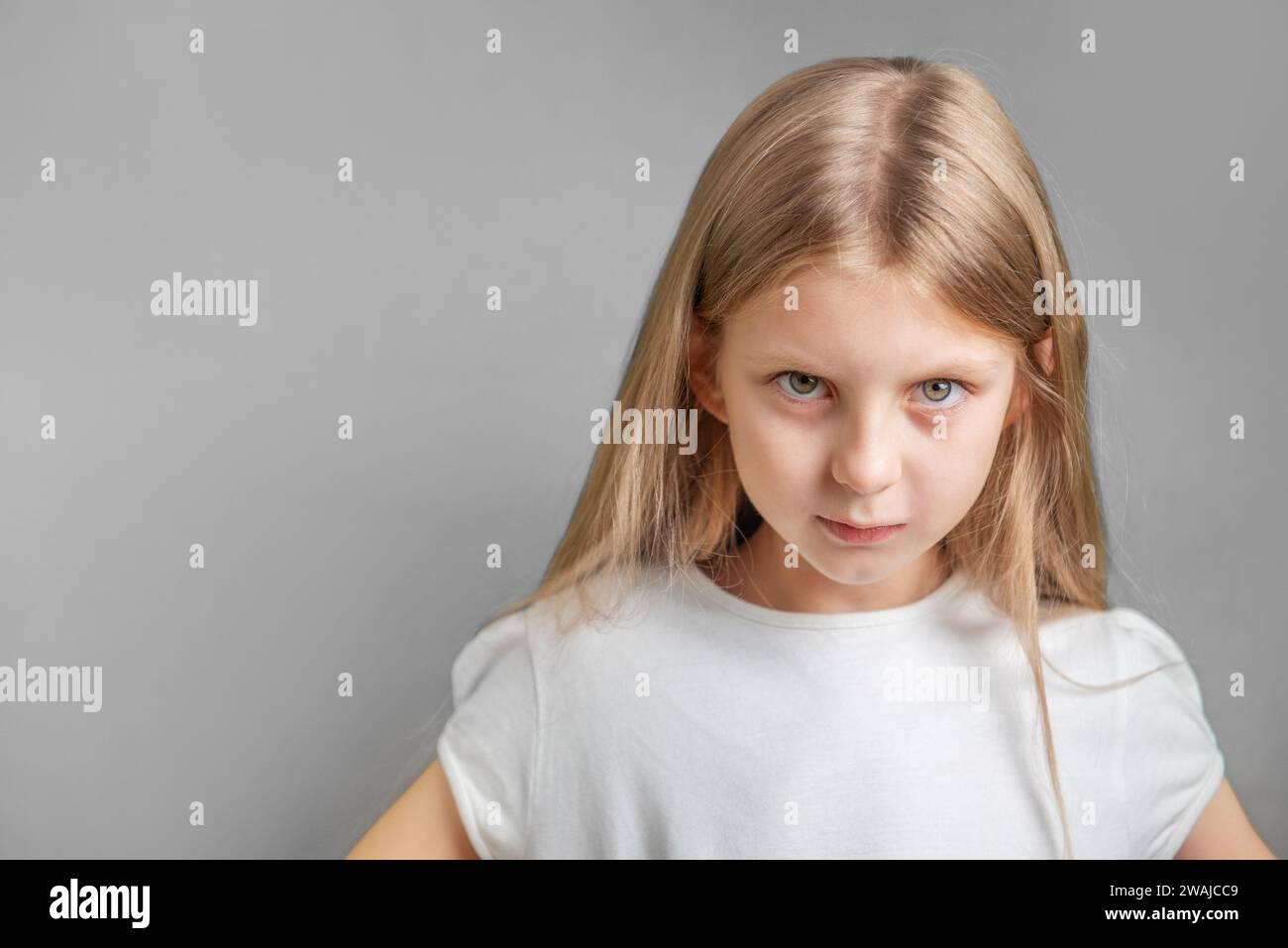 Ritratto di una bambina triste con t-shirt bianca su sfondo grigio Foto Stock