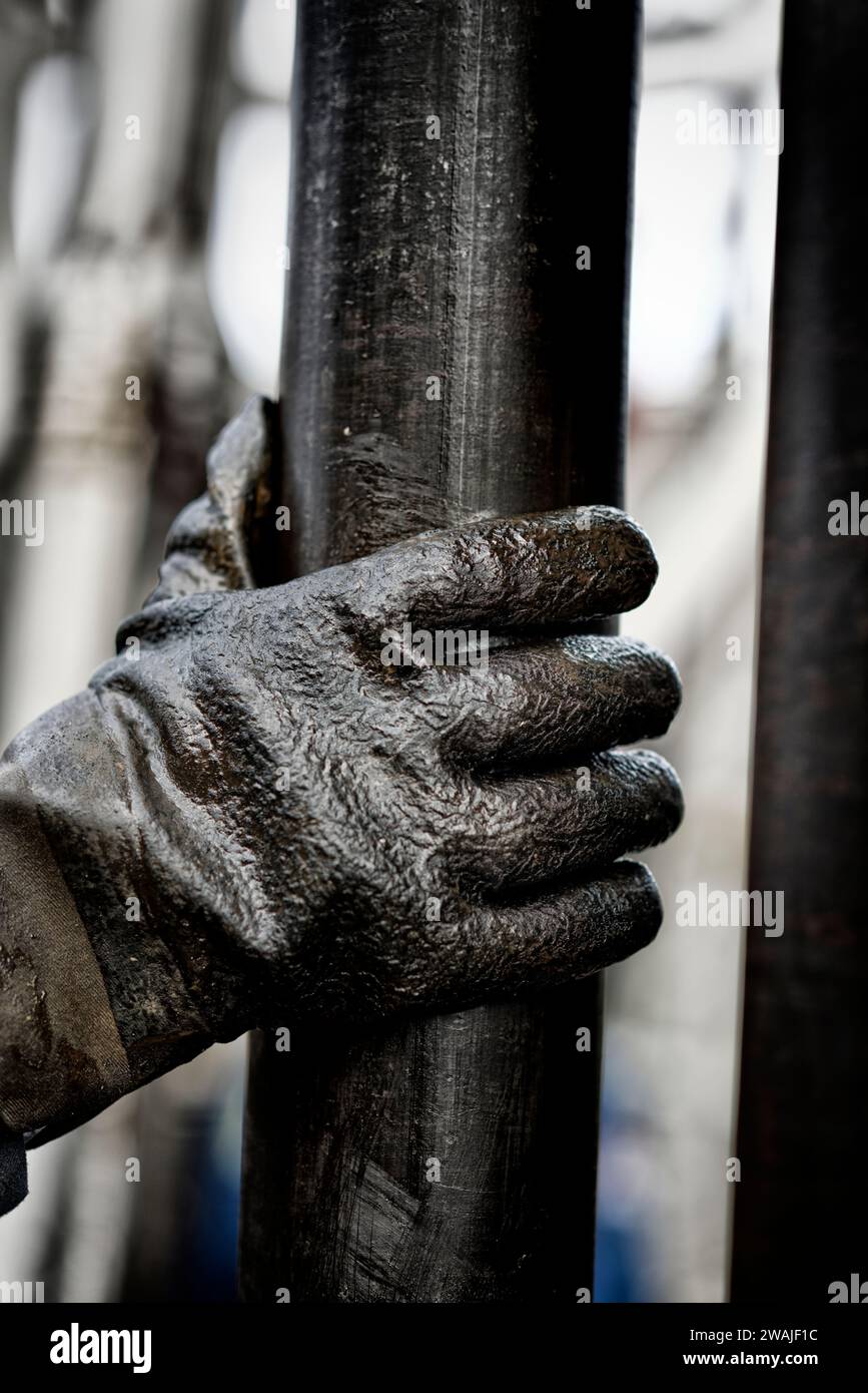 Una mano umana che indossa un paio di guanti su un tubo di perforazione oleoso Foto Stock