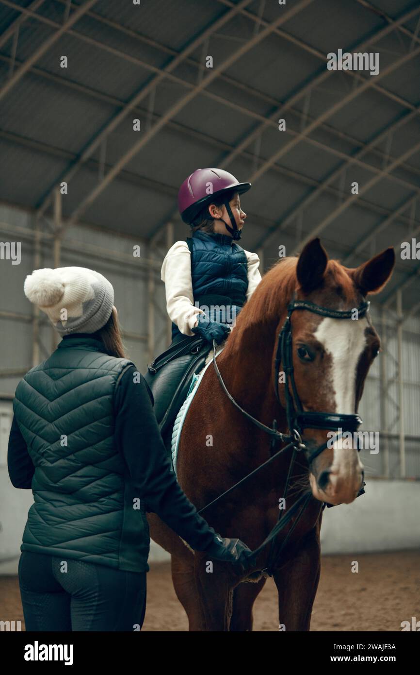 Istruttrice che insegna alla bambina, bambino che cresce a cavallo. Bambini che praticano passeggiate, dressage Foto Stock