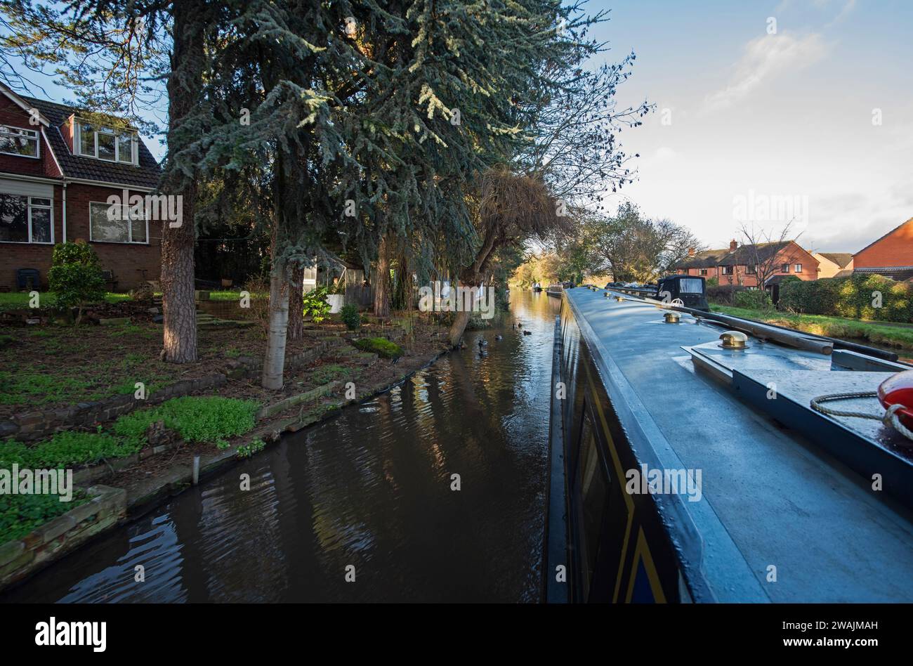 Vista da un narrowboat che viaggia nel paesaggio urbano della campagna inglese sul canale navigabile britannico attraverso il villaggio Foto Stock