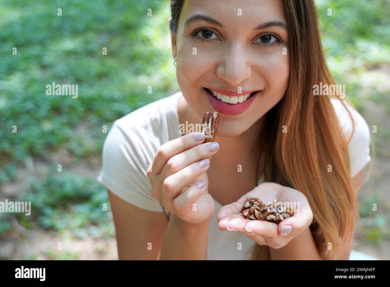 Primo piano di una donna sana che mangia noci pecan nel parco. Guarda la fotocamera. Foto Stock