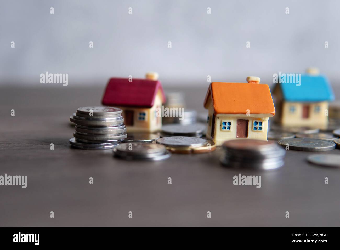 Immagine ravvicinata della casa dei giocattoli circondata da monete. Spazio di copia per il testo. Concetto di proprietà domestica. Foto Stock