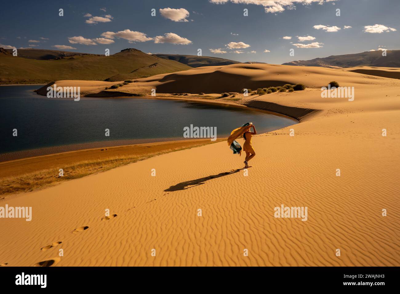 Una giovane donna cammina in oasi e dune sabbiose. Ragazza in abito giallo e lunga ombra nel deserto mongolo del Gobi Foto Stock