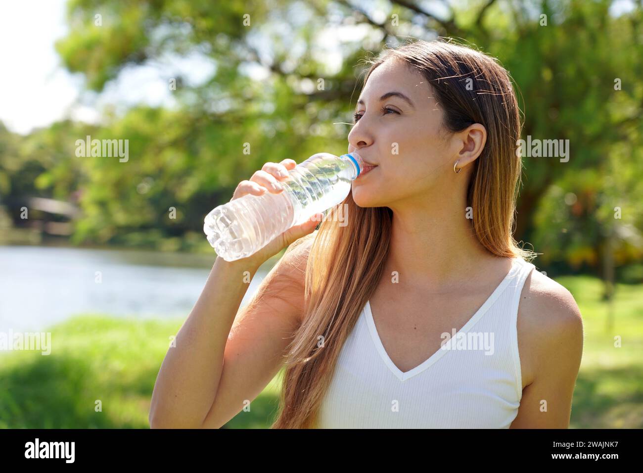 Donna fitness che beve acqua dalla bottiglia. Acqua potabile femminile caucasica brasiliana dopo esercizi o sport nel parco. Foto Stock