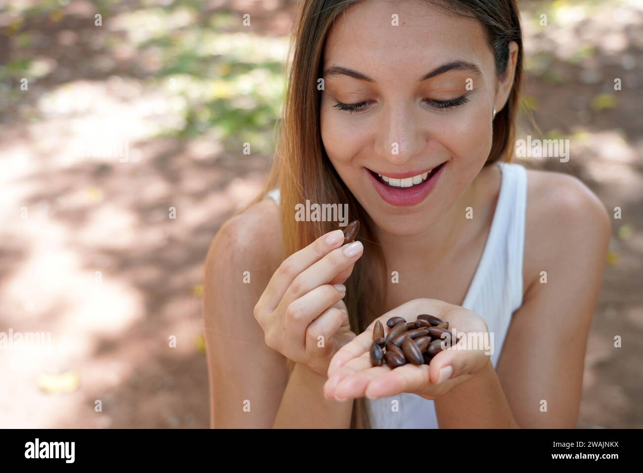 Bella ragazza sana che mangia semi di noci baru all'aperto. Guarda i semi di baru in mano. Foto Stock