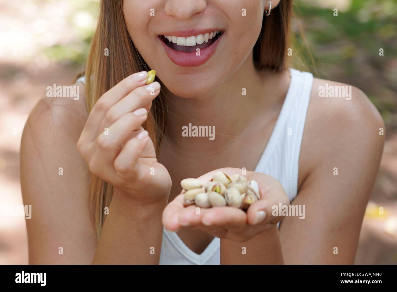 Fitness ragazza sana all'aperto. Primo piano di una giovane donna che mangia pistacchi nel parco. Concentrazione selettiva sulla sua bocca. Foto Stock