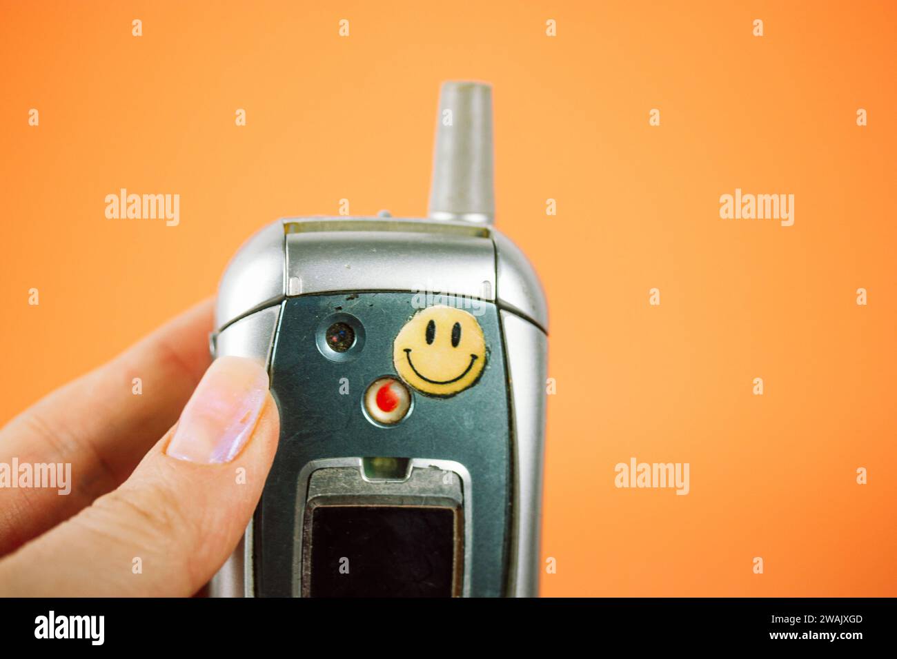 Madrid, Spagna. 2 gennaio 2024 vecchio telefono Motorola con adesivo sorridente in mano alla donna. Nostalgia per gli anni '90, '00 Mano che regge un telefono vintage. Foto Stock