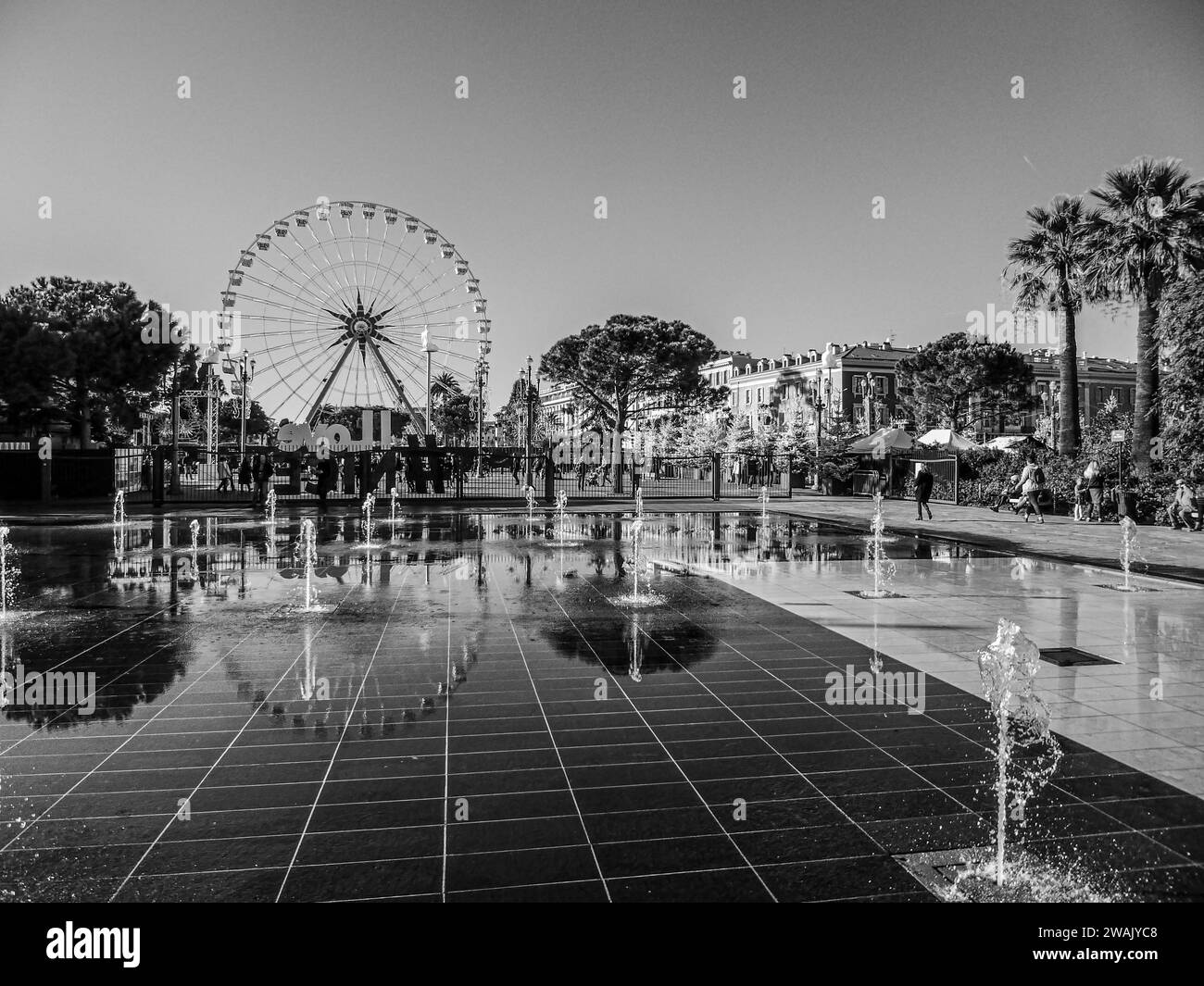 Una vista dall'alto di un iconico parco di divertimenti con una spettacolare ruota panoramica in bianco e nero, fontane illuminate e un lussureggiante paesaggio verde Foto Stock