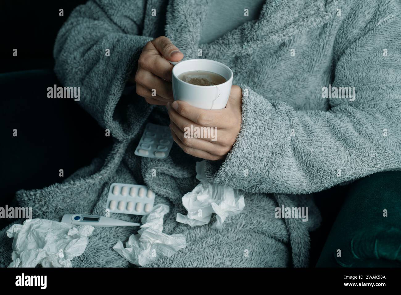 primo piano di un uomo malato a casa, che indossa un abito da casa grigio e si riscalda con una tazza di tè caldo alle erbe Foto Stock