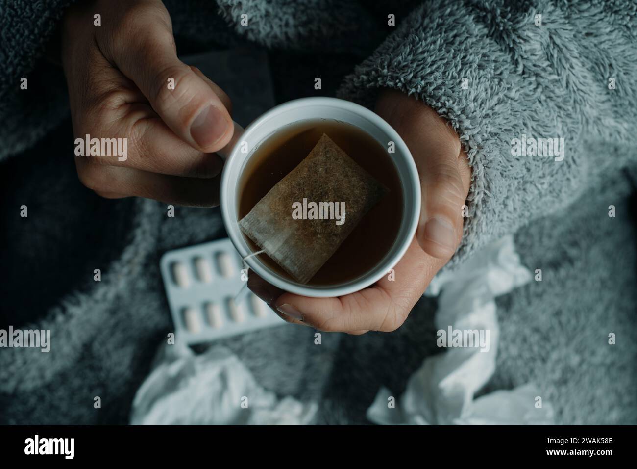 dettaglio di un uomo malato, che si riscalda con una tazza di tè caldo alle erbe, a casa, indossando un soffice abito grigio della casa, Foto Stock