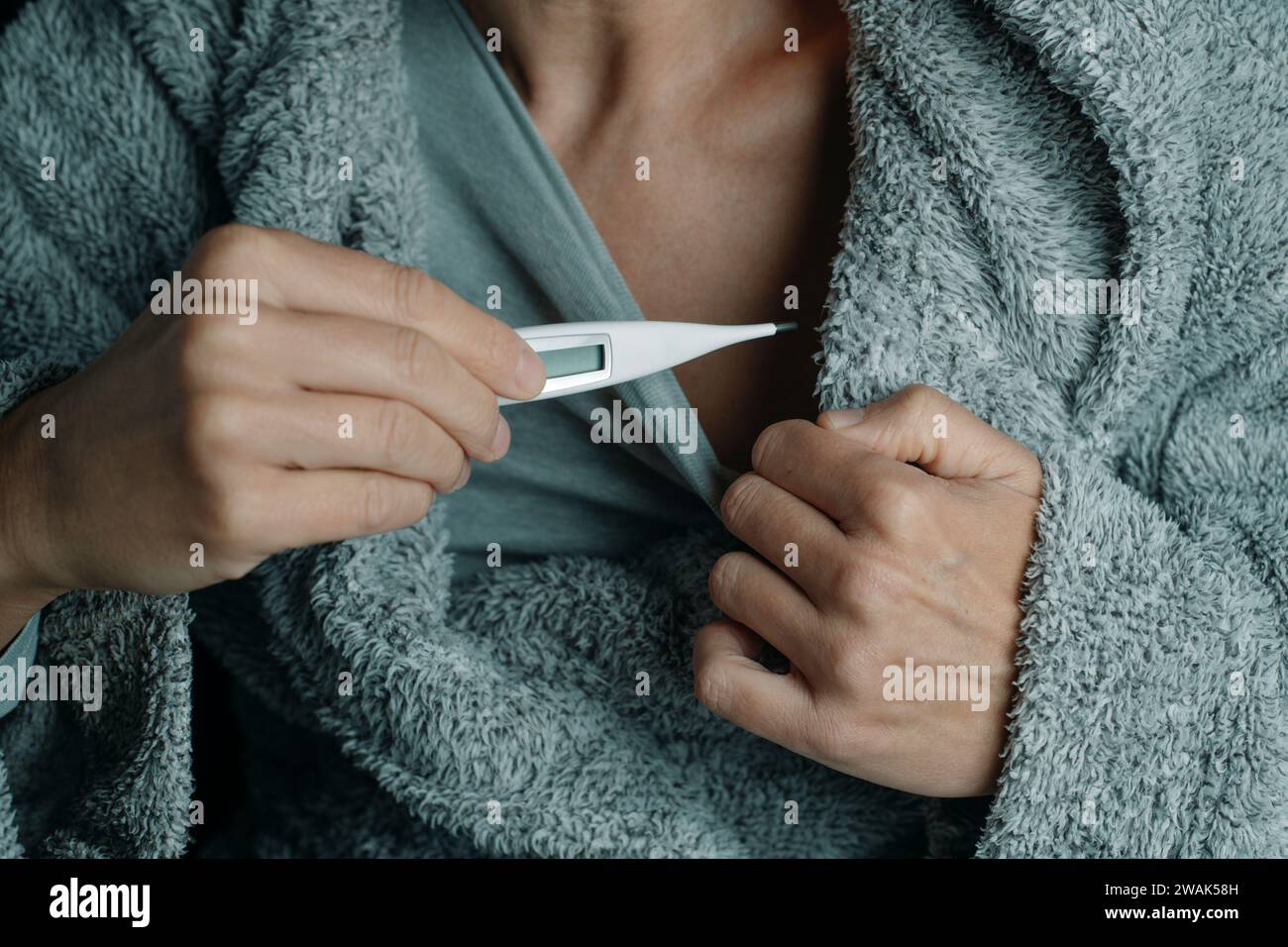 primo piano di un uomo malato, che indossa un soffice abito da casa grigio, a casa, sta per misurare la sua temperatura con un termometro digitale Foto Stock