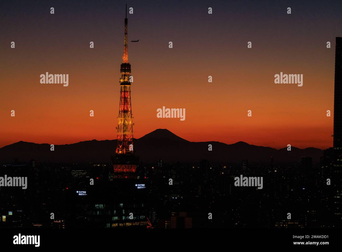 un aereo scende in un tramonto arancione mentre si avvicina alla torre di tokyo con la silhouette del monte fuji sullo sfondo Foto Stock